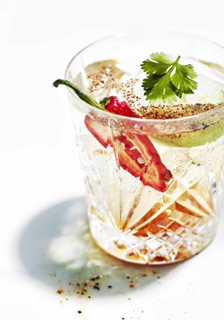 Spicy margarita with chili pepper garnish and textured salt rim in detailed glassware, photographed for beverage marketing.