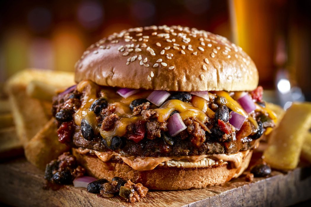 a burger with beans and cheese on a wooden board