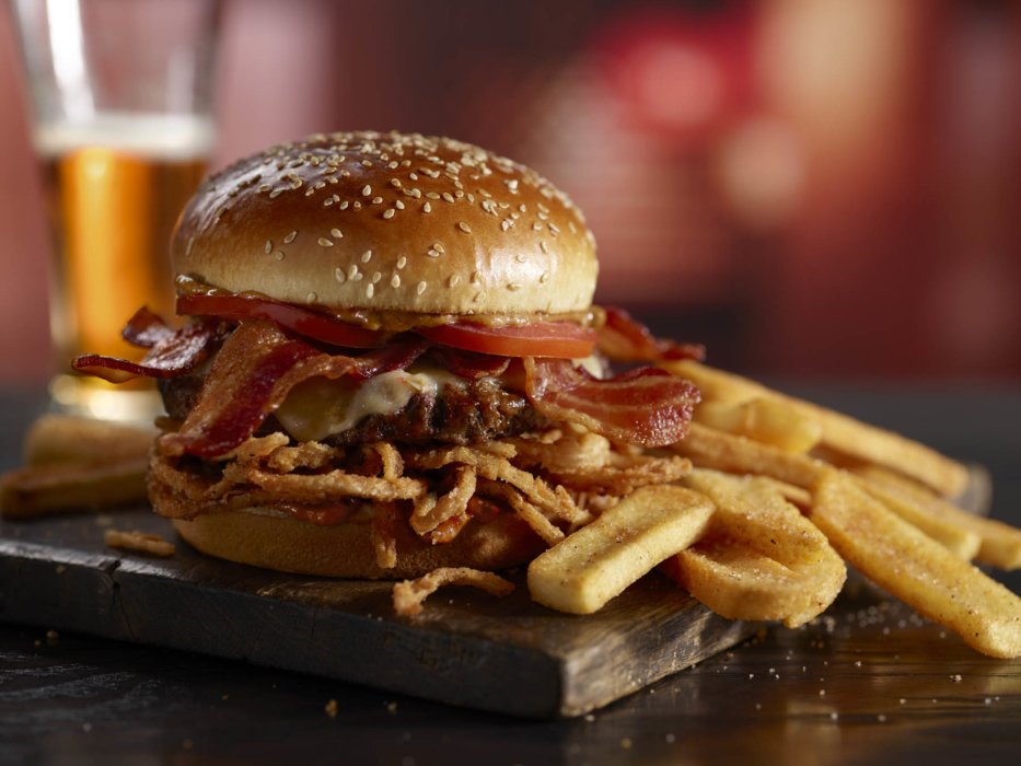 a burger with bacon and fries on a wooden board
