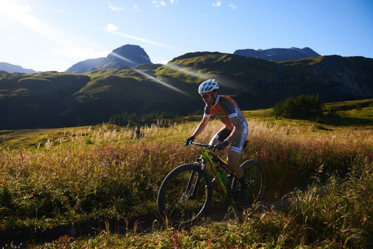 A cyclist riding through a beautiful field in a mountain range - bike photo