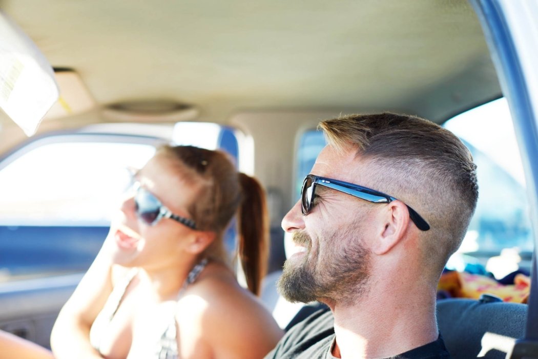 Two people smiling in their car wearing sunglasses laughing in a car