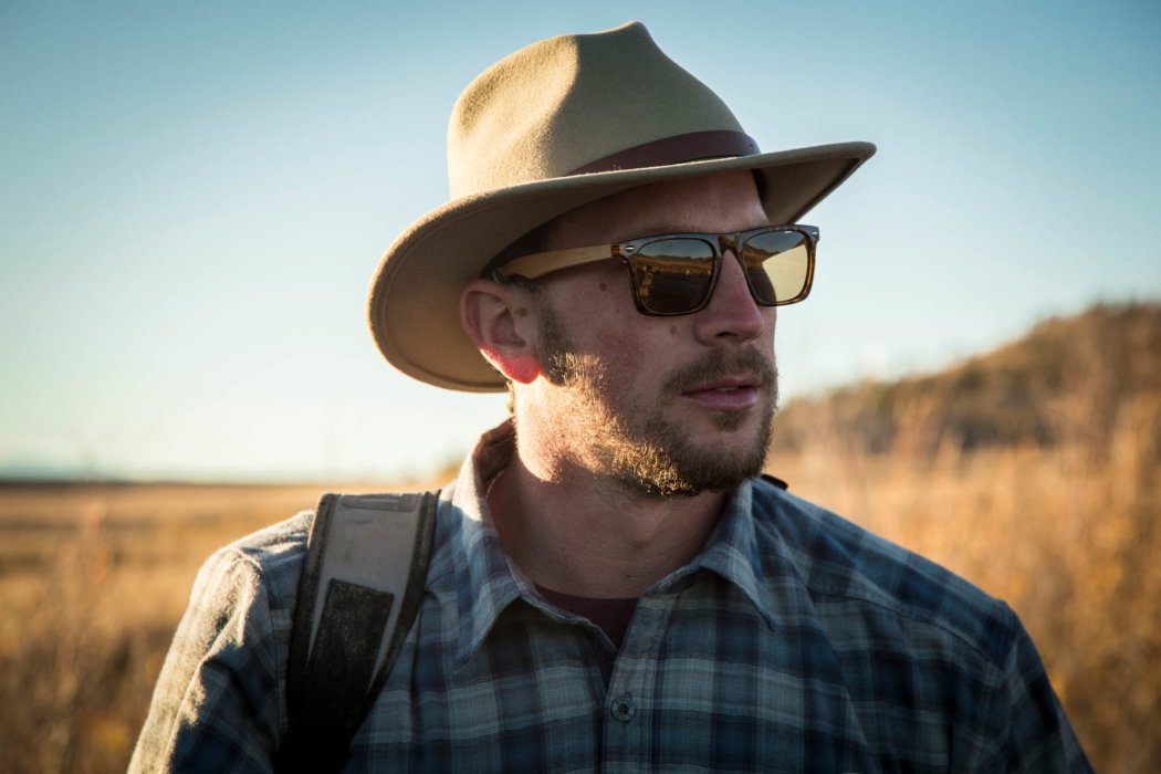 A man wearing sun glasses and an fedora going on a hike
