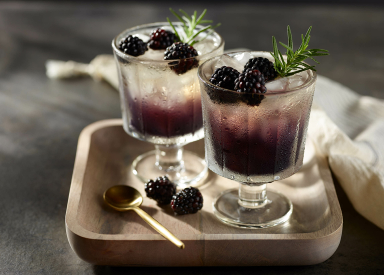 Layered blackberry cocktail with rosemary garnish in stemmed glasses – commercial beverage photography by OMS Photo.