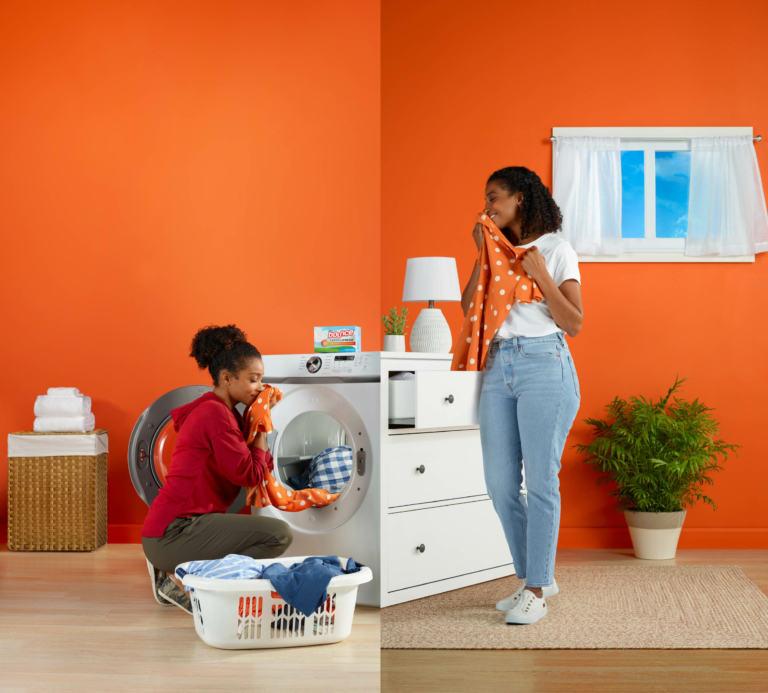 Mother and young child in a bright laundry room using P&G cleaning products with orange wall background