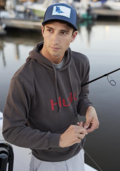 Man wearing a hoodie while fishing, holding a fishing rod near water