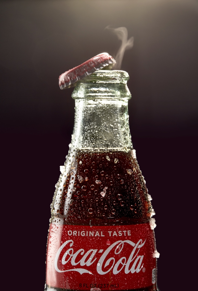 Glass soda bottle with condensation and lifted cap captured in commercial beverage photography studio