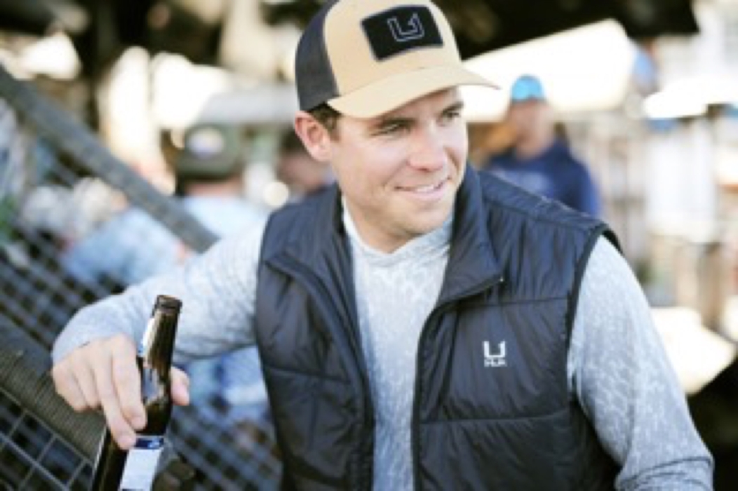 Man wearing a branded vest holding a drink in an outdoor lifestyle setting