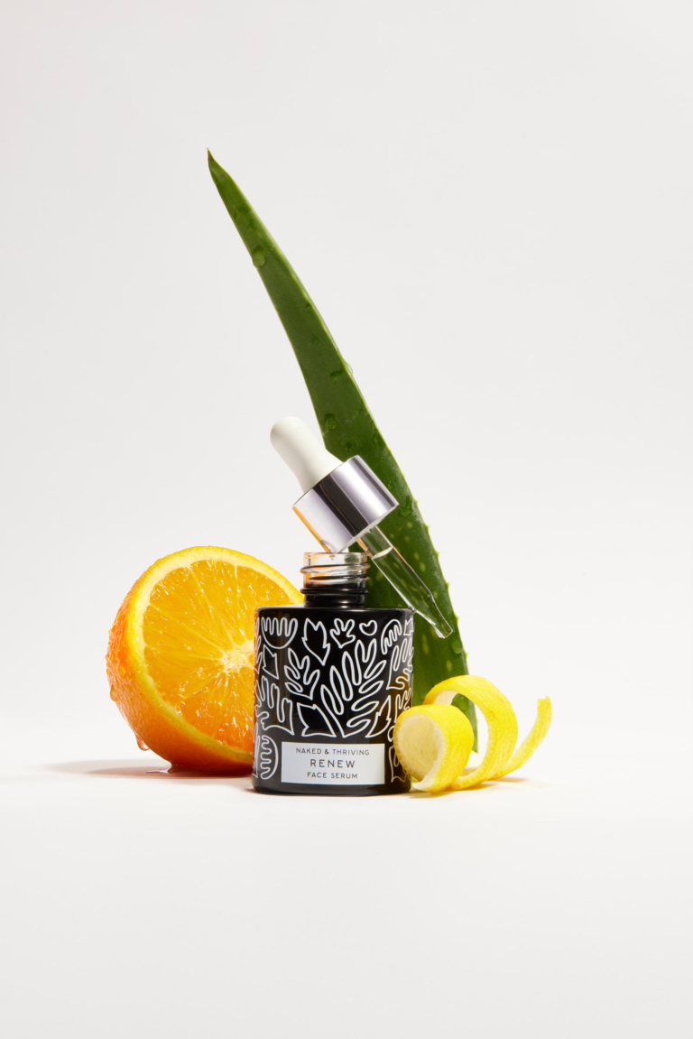 Naked & Thriving facial oil bottle with fresh orange slices and aloe vera leaf on white background