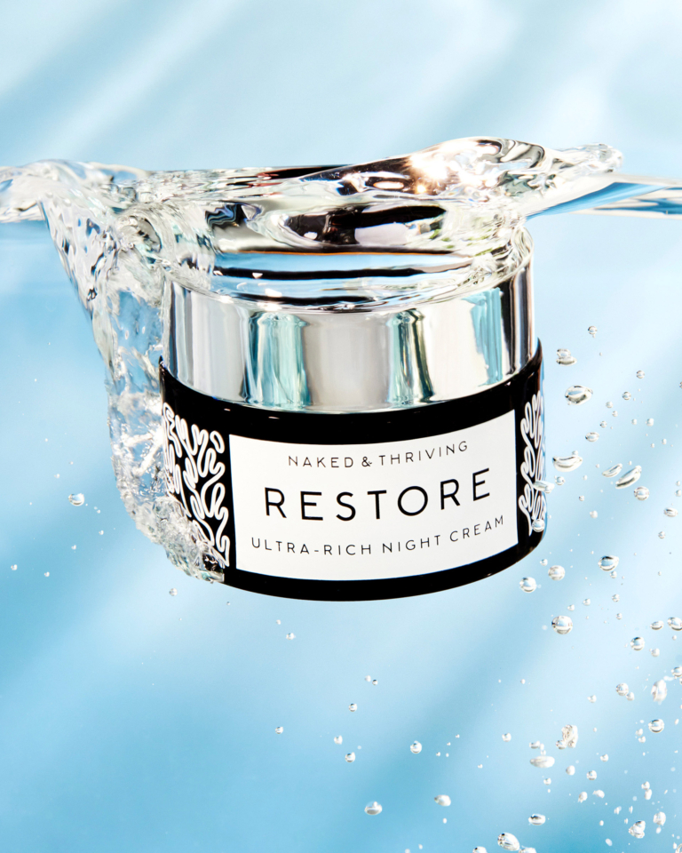 Naked & Thriving Restore ultra-rich moisturizer jar splashing in water on bright blue background