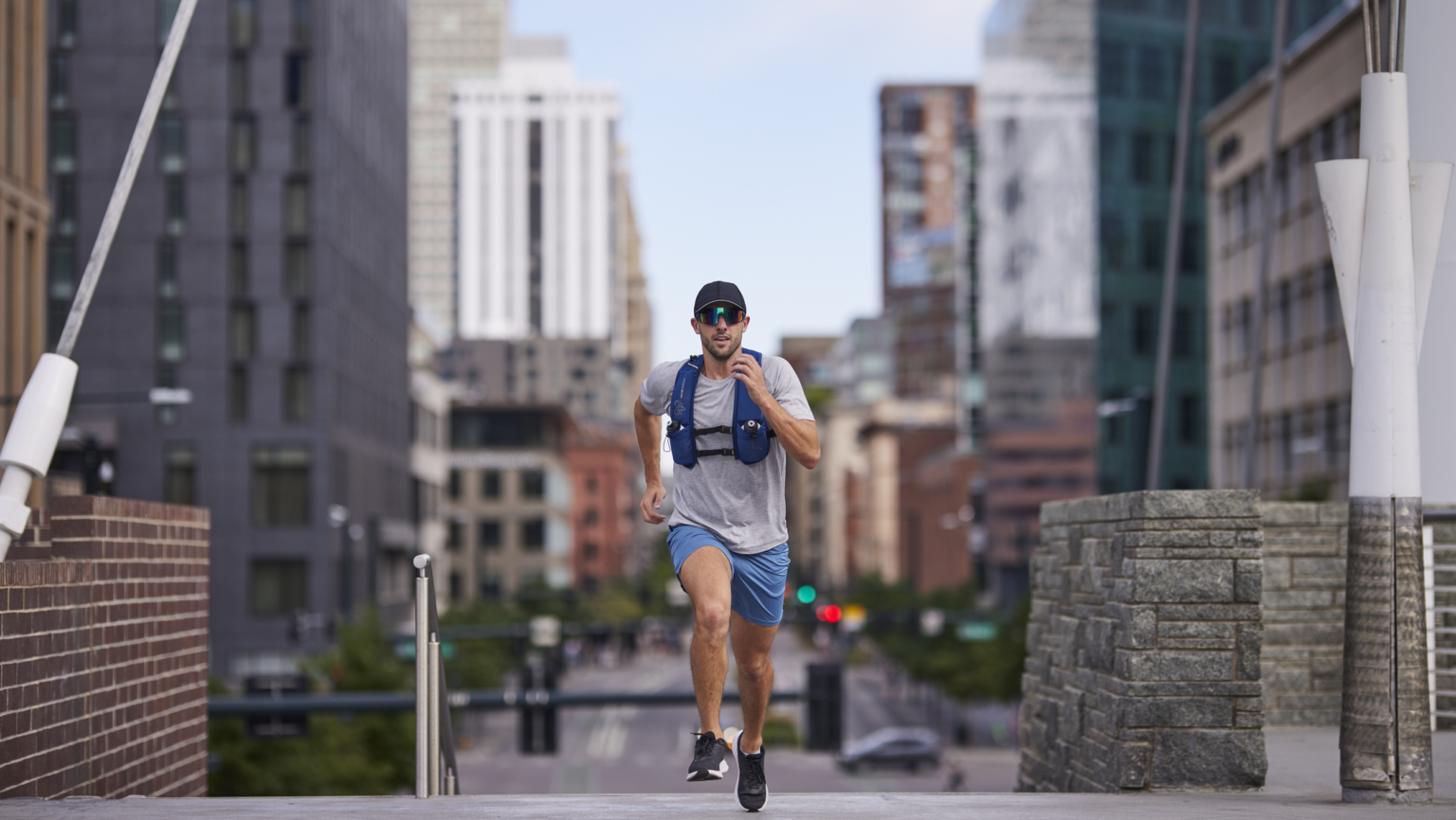 Runner wearing a hydration vest and performance gear running through a downtown city environment, athlete photography by Monty Milburn
