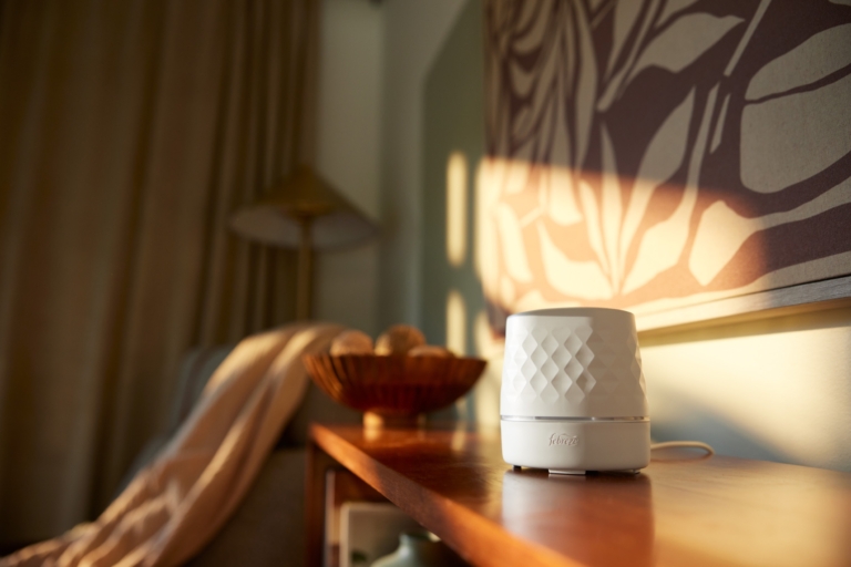 White Febreze plug-in air freshener diffuser on a nightstand in a warmly lit bedroom
