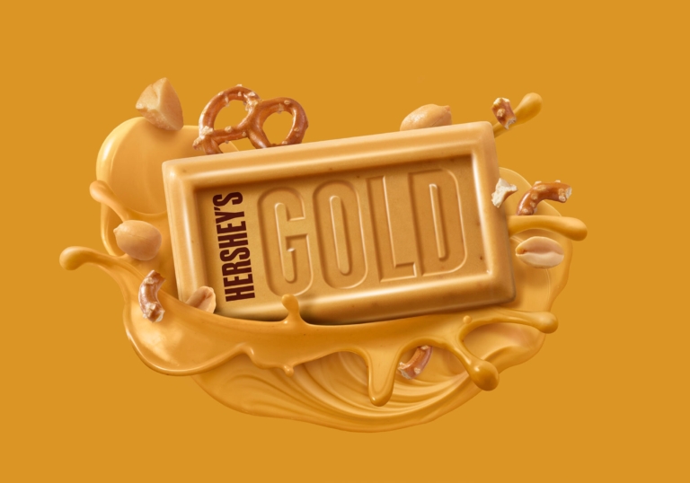 Hershey’s Gold candy bar surrounded by caramelized crème, pretzels, and peanuts splashing outward.