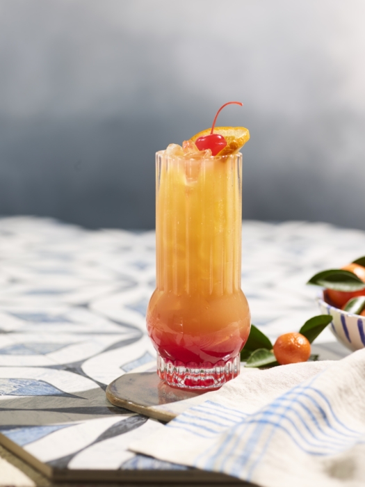 a glass of orange and red liquid with a cherry on top