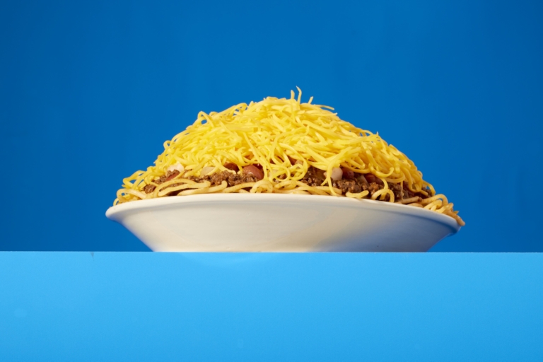 Plate of Skyline Chili 3-Way spaghetti piled high with shredded cheddar cheese on a solid blue background.