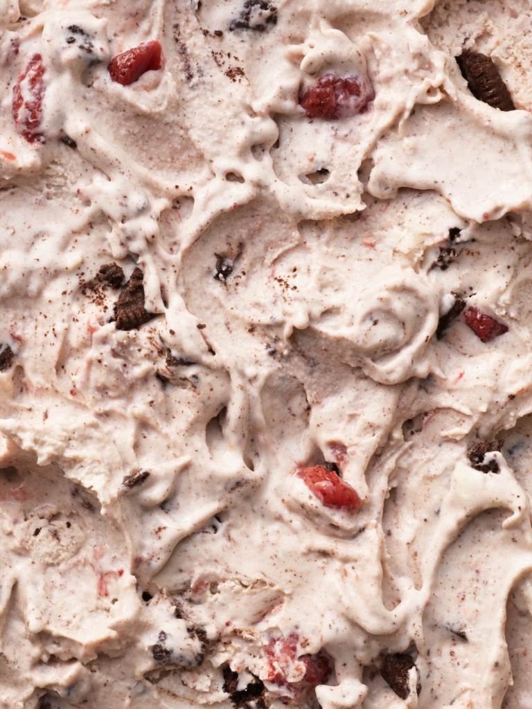 Macro texture shot of strawberry ice cream with chunks and mix-ins swirled throughout.