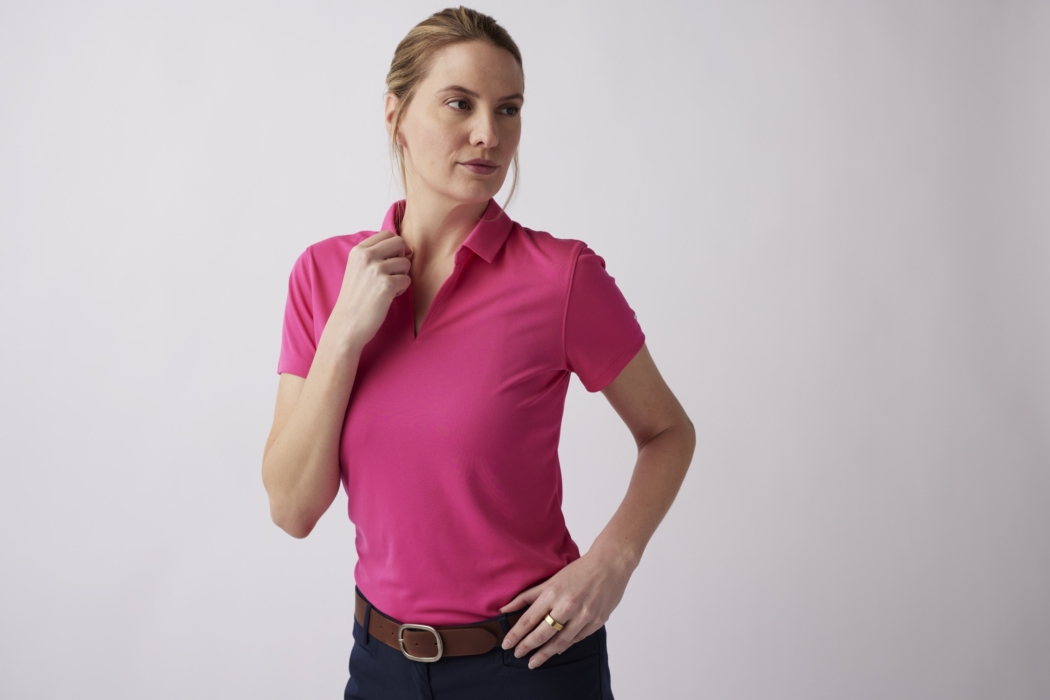 Woman wearing a pink polo shirt adjusting collar in a clean studio setting