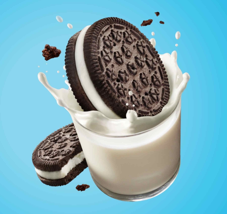 Chocolate sandwich cookie falling into a glass of milk with splashes on a bright blue background.