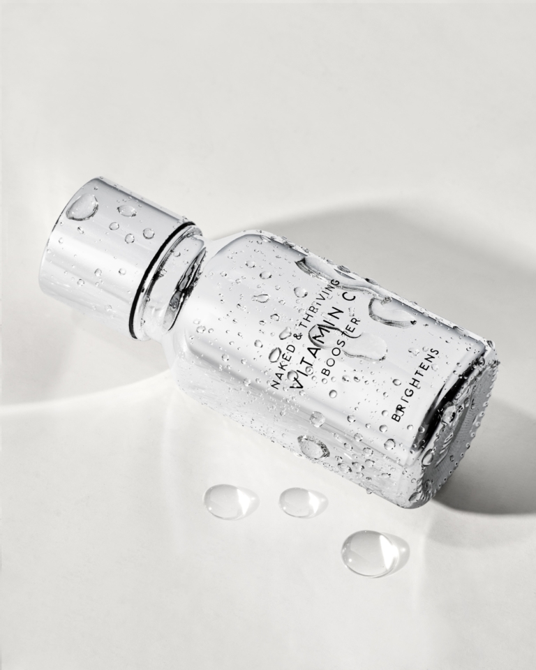 Naked & Thriving face serum bottle lying on white surface with water droplets