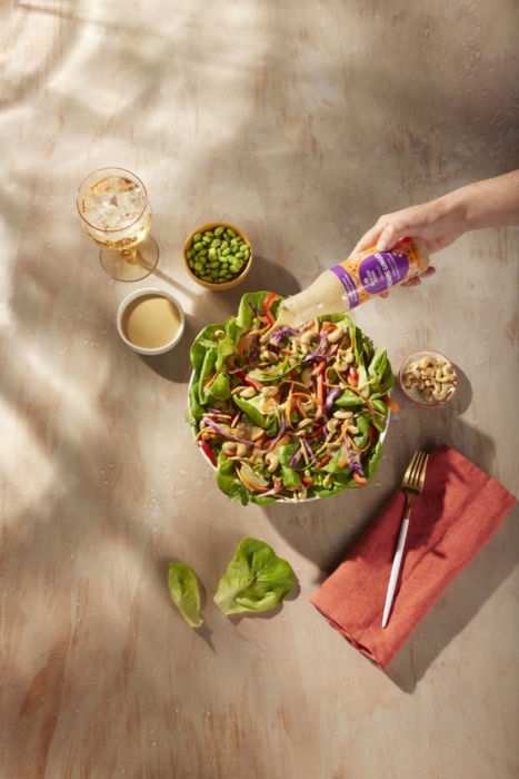a hand pouring a bottle into a salad