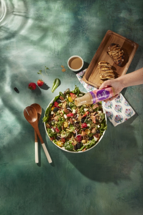 a hand pouring a bottle of juice into a bowl of salad