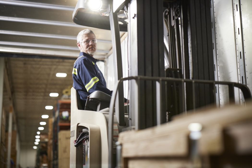 a man in a blue shirt and glasses sitting in a forklift, Cintas, construction, workplace, jobsite, on location