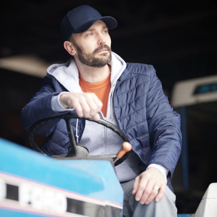 a man in a hat and jacket sitting on a tractor, Cintas, construction, workplace, jobsite, on location