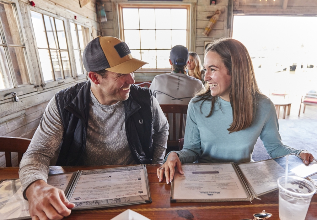Couple in HUK outdoor gear enjoying a meal and placing order at casual restaurant, photographed for lifestyle and crossover apparel marketing by OMS Photography