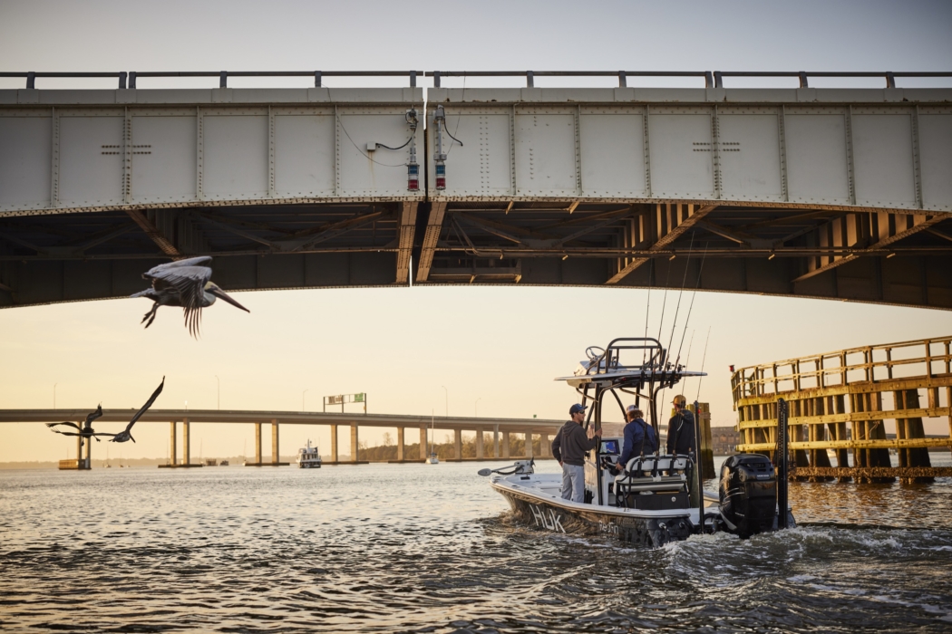 Distant view of men on a HUK-branded boat heading into the sunset, captured for outdoor adventure and fishing lifestyle photography by OMS Photography