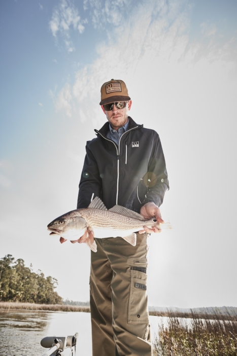 Man holding freshly caught fish while wearing HUK performance gear, captured for outdoor adventure and fishing lifestyle photography by OMS Photography