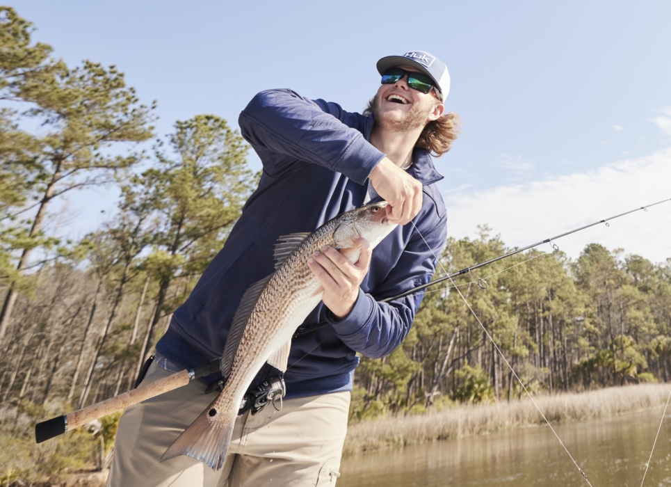 Man holding freshly caught fish while wearing HUK performance gear, captured for outdoor adventure and fishing lifestyle photography by OMS Photography