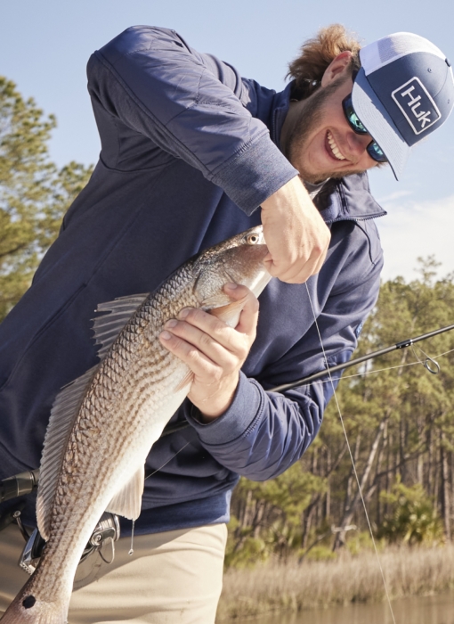 Man holding freshly caught fish while wearing HUK performance gear, captured for outdoor adventure and fishing lifestyle photography by OMS Photography