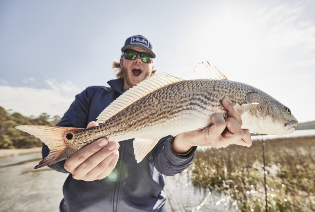 Man holding freshly caught fish while wearing HUK performance gear, captured for outdoor adventure and fishing lifestyle photography by OMS Photography