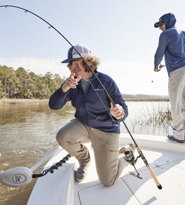 Two men wearing HUK fishing gear casting lines in outdoor setting, captured for adventure and lifestyle brand photography by OMS Photography