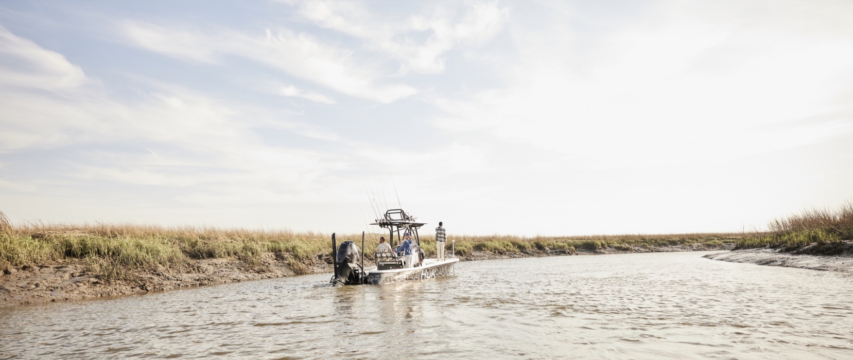 Wide shot of three anglers on a boat surrounded by open water and natural landscape, captured for outdoor lifestyle and fishing campaigns by OMS Photography