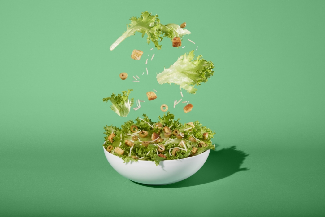 a bowl of salad with lettuce and croutons falling