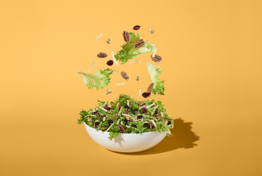 a bowl of salad with nuts falling