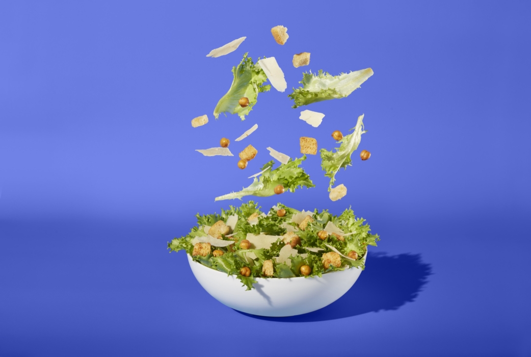 a bowl of salad with croutons falling