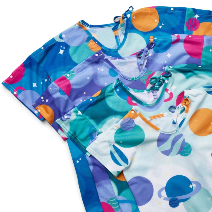 Close-up studio image of pediatric hospital gowns on white background by Marci Rhodes of OMS Photography – detailed textile shot highlighting fabric texture, stitching, and playful patterns.
