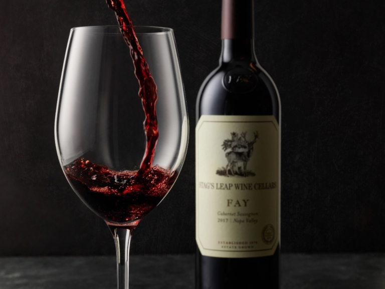 Wine being poured into a glass with bottle in background, sharp studio photography on dark backdrop for advertising by OMS Photography
