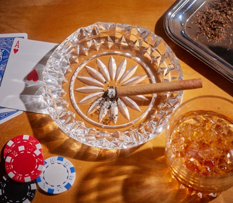 a cigar in a crystal ashtray with a drink and chips