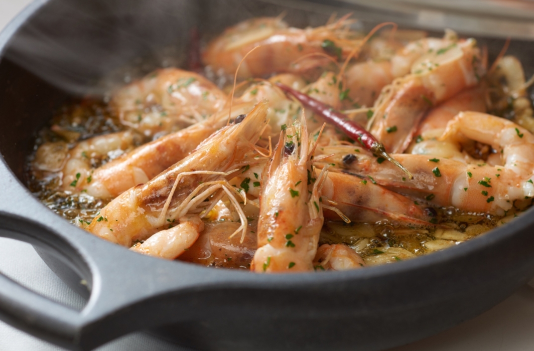 Shrimp simmering in a skillet with garlic, herbs, and chiles, photographed by OMS Photo, expert commercial food photographer.
