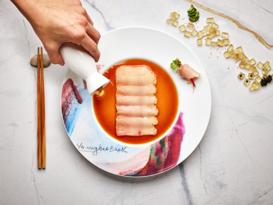 Hand pouring sauce over plated hamachi crudo on an artistic dish, photographed by OMS Photo, expert commercial food and fine-dining photographer.
