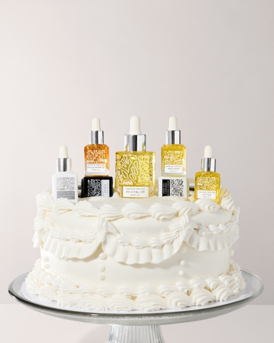 Naked & Thriving facial oil collection bottles displayed on white frosted cake on white background