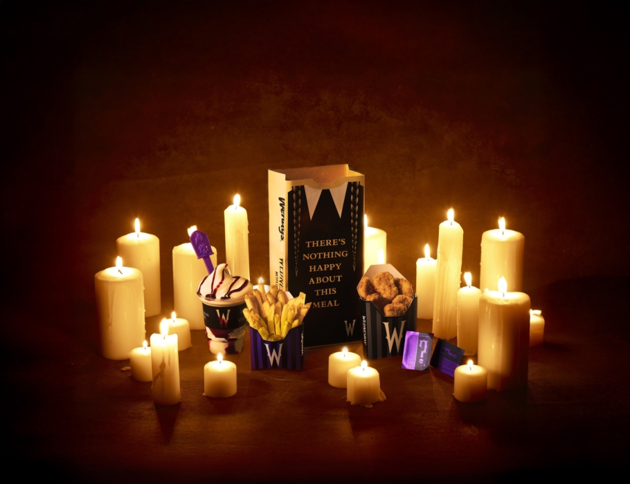 Fast-food fries, desserts, and packaging arranged around glowing candles on a dark warm-toned background for a Halloween theme.