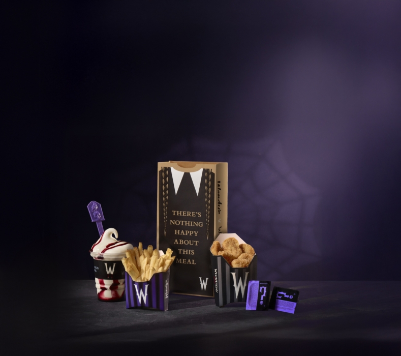 Halloween-themed display of fast-food fries, desserts, and packaging with purple lighting and a spiderweb backdrop.