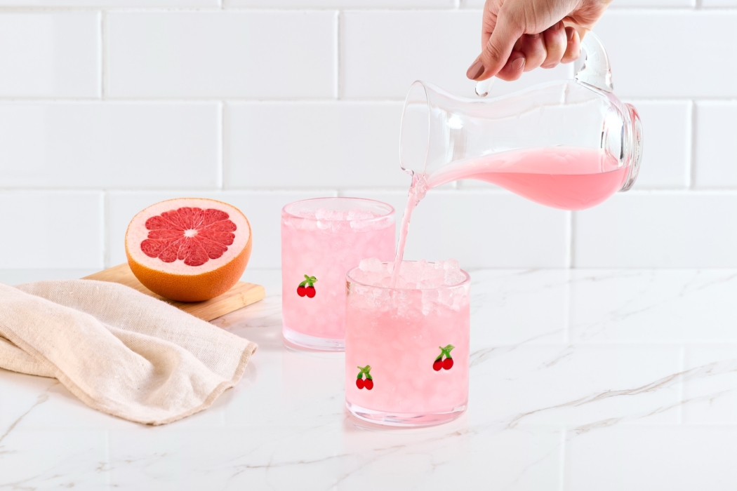 Pink lemonade being poured into glass with strawberry garnish in bright lifestyle beverage setup