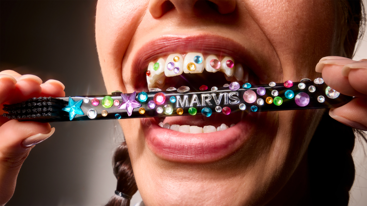 Close-up of a woman biting a gemstone-covered Marvis toothbrush, revealing rhinestone-covered teeth in a playful, surreal setup.
