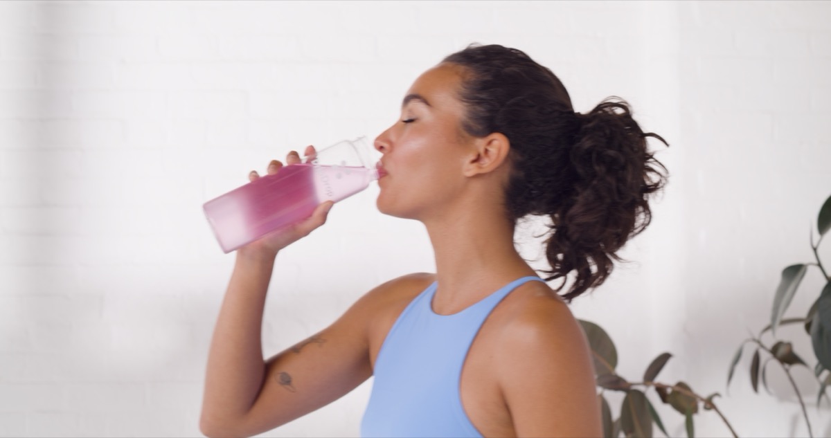 Female model drinking pink functional beverage photographed in bright lifestyle setting for commercial advertising