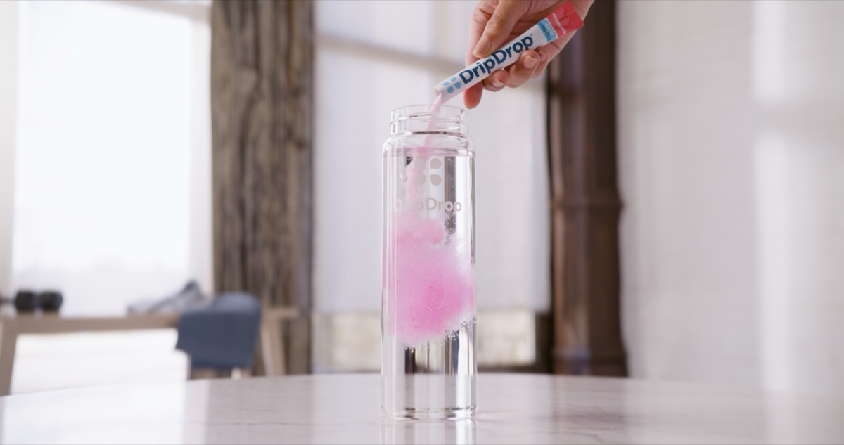Pink hydration powder being poured into clear water bottle captured in commercial beverage photography studio