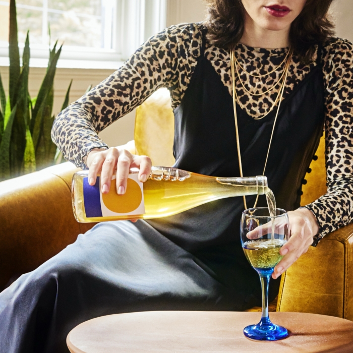 Woman pouring yellow cocktail from bottle into blue stem glass captured in commercial beverage lifestyle photography